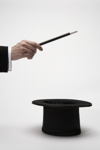 Man holding magic wand over top hat, close-up of hand, side view