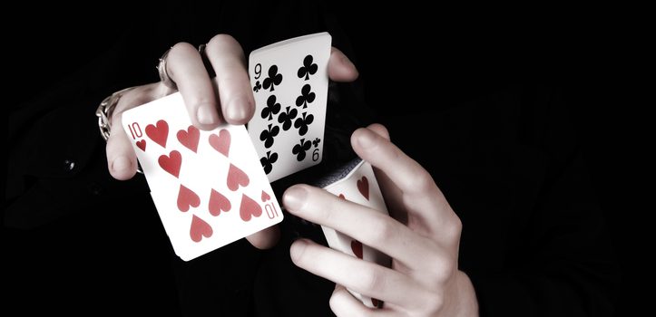 Young magicians hands holding a lot of play cards. black background